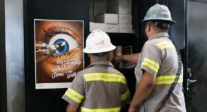 Two factory workers at lockers, next to Alchemy poster about eye injuries